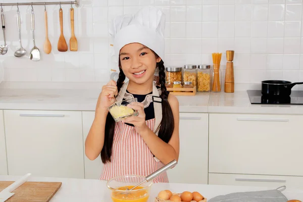 Cute little Asian cooking student chef  learning cooking savory dishes in the kitchen. Prepare spices and pepper in an egg bowl : Cooking and nutrition learning concepts at cooking school.