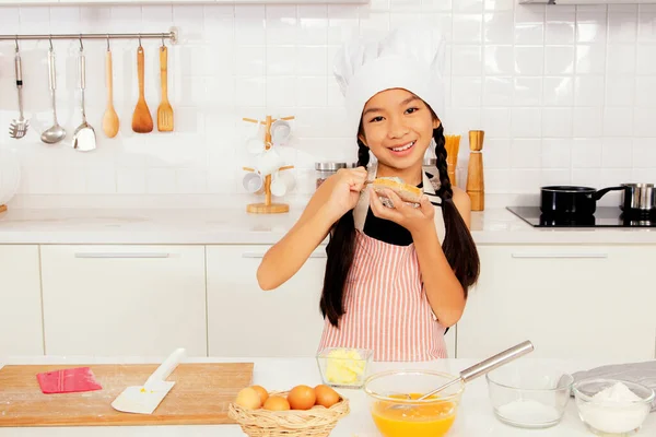 Cute little Asian cooking student chef  learning cooking savory dishes in the kitchen. Prepare spices and pepper in an egg bowl : Cooking and nutrition learning concepts at cooking school.