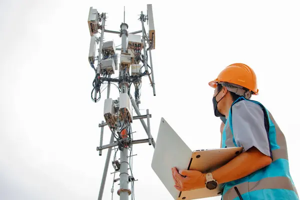 Hjälmförsedd Asiatisk Manlig Ingenjör Arbetar Fält Med Telekommunikationstorn Som Styr Royaltyfria Stockbilder