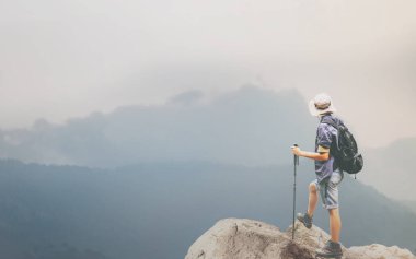 Genç adam, sırt çantasıyla gezerken, bastonla gezerken, başarıyla yürürken, yüksek dağlarda, kayaların üzerinde dikilirken, güzel dağ manzarasına bakarken, dumanla ve taze sabah havasıyla, zengin doğaya bakarken..