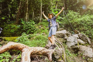 Neşeli genç adam, dağlarla, şelalelerle ve yemyeşil ormanlarla tropikal ormanlarda yürüyüş yapmayı seviyor. Kütüğün üzerinde dikilip güzelliği ve temiz havayı seyrediyor..