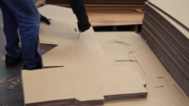 Erkek işçi, kağıt paketleme endüstrisinde paketlemek için karton kutularda delikler açmak için özel bir araç kullanır.