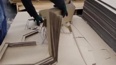 Erkek işçi, karton çarşaf yığınından kesilmiş yığını kaldırır. Geriye sadece kutu ürünleri yapmak için katlanmış karton kutular bırakır ve kağıt ambalaj endüstrisi için onları sınıflandırır..