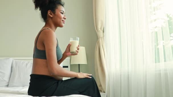 若い母親タイ アフリカ系子孫は 飲み物のパスツール化されたミルクの健康治療を準備する彼女の寝室に座って 筋肉と骨の妊婦を強化し 栄養カルシウム強度の胎児を増加させる — ストック動画