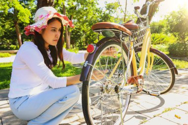 Bisiklet şapkası takan Asyalı kadın botanik bahçesinde yemyeşil ve gölgeli ağaçlarla oturuyor ve lastiğin yumuşak olmasını engellemek için önce lastik basıncını kontrol ediyor..