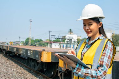 Teftiş bölgesinde çalışan güzel Asyalı kadın teknisyen dizel tren, ham petrol nakliye demiryolu tren istasyonunda elinde tablet ve miğferle tamir atölyesine gidiyor..