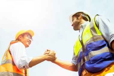 İki mühendisin başarısı: Kafkas erkek mimar ve Asyalı mühendis el sıkışması endüstriyel iş projeleri planlamasında olumlu yaklaşıma inanan bir ekipte iş arkadaşı olarak çalışıyorlar.