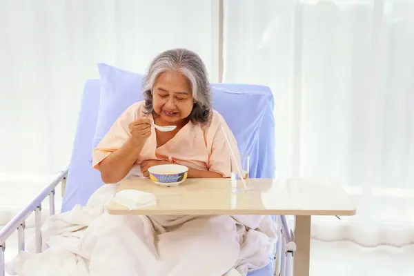 Senior female asian patient sits and eats porridge soft food appetizing that is easy to digest and easy to eat suitable for both elderly patients while recovering from illness in the hospital.