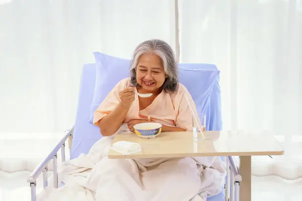 Senior female asian patient sits and eats porridge soft food appetizing that is easy to digest and easy to eat suitable for both elderly patients while recovering from illness in the hospital.