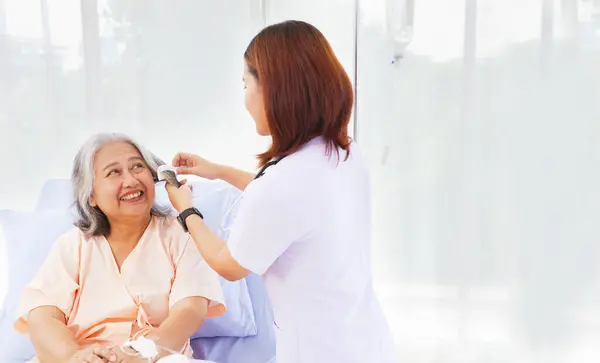 Female nurse takescare health friendly elderly patients help with willingness comb gray hair encourage patient feel good and give encouragement help in recuperating from illness in the hospital.