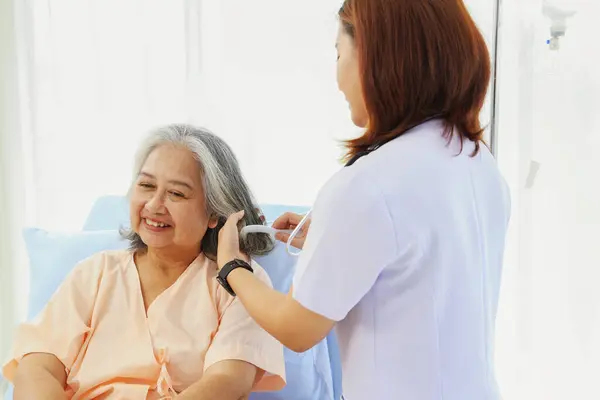 Female nurse takescare health friendly elderly patients help with willingness comb gray hair encourage patient feel good and give encouragement help in recuperating from illness in the hospital.