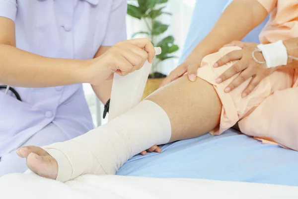 통증을 환자를 돌보는 간호사의 간호사의 통증을 붕대를 사용하여 환자의 침대에서 스톡 사진
