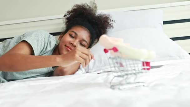 健康な妊娠したアフリカ系アメリカ人の母親は 迅速かつ簡単なショッピングカートでオンラインで注文した子供の赤ちゃんの靴を見て自宅のベッドに横たわっています — ストック動画