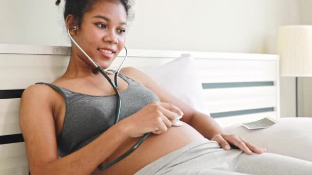 妊娠中のタイ アフリカ系アメリカ人の母親は 胎児の心拍を聞き 赤ちゃんが胎内に移動したときに興奮してベッドに超音波画像を置きました — ストック動画