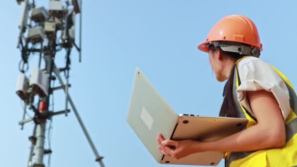亚洲女工程师头戴安全帽 用手提电脑进行现场工作电信塔控制移动电力安装 — 图库视频影像