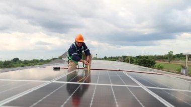 Mühendis elektrikçi Asya, endüstriyel tesislerdeki metal çatılara güneş panelleri kurulumunu kontrol ediyor. Güneş panellerinin uzunluğunu ölçmek için bir mezura kullanın ve veriyi bir tablete kaydedin.