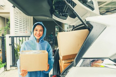 Asyalı iş kadını internetten teslimat yapıyor. Toptan satış siparişi veriyor. Yağmurluk giyiyor, yağmur mevsiminde evin önündeki müşterilere paket kutuları teslim ediyor..