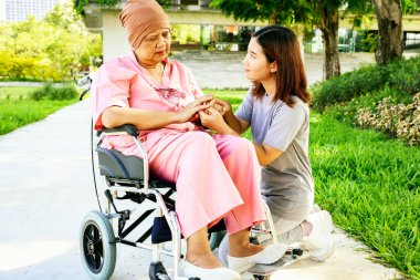 Kızı, kanserden hasta olan ve hastanede tedavi gören yaşlı annesinin elini tutarak oturuyor. Kızının ona bağlandığı için duyduğu minnettarlık iyileşme umuduyla ona destek oluyor..