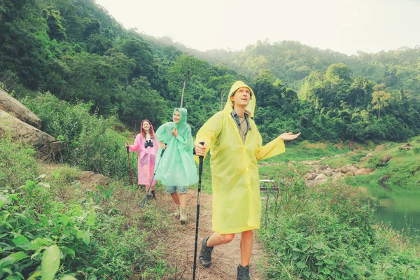 Group caucasian men and women traveling in the rainy season and wearing raincoats travel through the tropical forests Thailand using trekking sticks steep nature trails in search beautiful waterfalls.