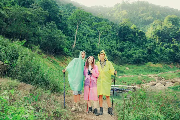 Group caucasian men and women traveling in the rainy season and wearing raincoats travel through the tropical forests Thailand using trekking sticks steep nature trails in search beautiful waterfalls.