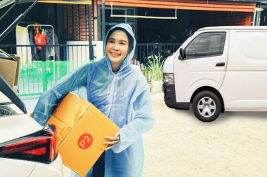 Asyalı iş kadını internetten teslimat yapıyor. Toptan satış siparişi veriyor. Yağmurluk giyiyor, yağmur mevsiminde evin önündeki müşterilere paket kutuları teslim ediyor..