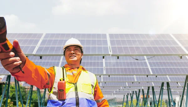 Senior male worker electrical technician hands electric drill to colleague at solar cell station work site inspect repair and maintenance plan for solar cell panel farm eco technology solar panels.