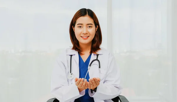 Female volunteer doctor surgeon in portrait in white uniform with gentle medical stethoscope sits chair in the office relaxes smiling at the camera friendly giving good wishes happiness to everyone.