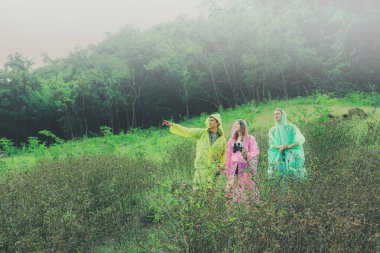 Yağmur mevsiminde seyahat eden ve yağmurluk giyen beyaz erkek ve kadınlar, Tayland tropikal ormanlarında yürüyüş çubukları kullanarak güzel şelaleleri aramak için doğa patikalarını kullanırlar..