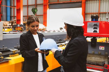 Kadın fabrika müdürü güvenlik kaskını memnuniyetle teslim ederken aynı zamanda kadın iş kadını ve iş ortağını da metal levha sektöründe güvenlik için bir tura çıkarıyor..