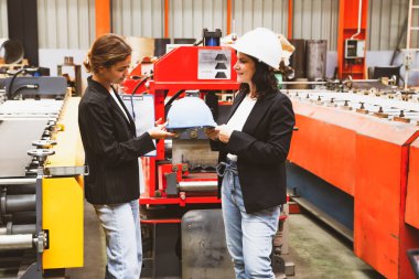 Kadın fabrika müdürü güvenlik kaskını memnuniyetle teslim ederken aynı zamanda kadın iş kadını ve iş ortağını da metal levha sektöründe güvenlik için bir tura çıkarıyor..