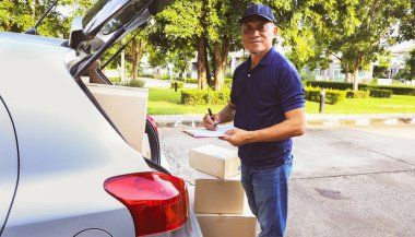 Ev teslimatı: Son sınıf erkek çalışanı kamyonun arkasında duruyor, müşterinin paket teslimat listesini ve karton kutu ürünlerini doğru teslimat için bir panoya kaydediyor..