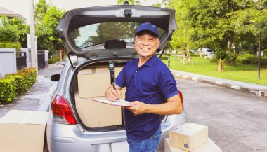 Ev teslimatı: Son sınıf erkek çalışanı kamyonun arkasında duruyor, müşterinin paket teslimat listesini ve karton kutu ürünlerini doğru teslimat için bir panoya kaydediyor..