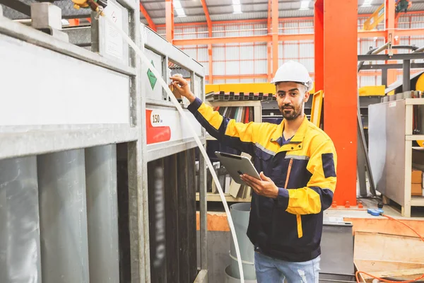 Male safety worker in a hard hat holds tablet inspecting oxygen gas tanks and checking pressure for metal cutting work in a safe storage floor in a metal roofing factory.