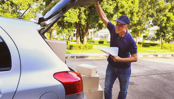 Ev teslimatı: Son sınıf erkek çalışanı elinde teslimat listesiyle karton kutu kamyonu açıyor ve müşterileri evin önünde paketlemeye hazırlanıyor..