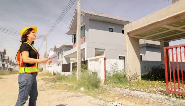 Üst düzey kadın mimar proje tasarısını elinde tutuyor. Projenin önündeki inşaat sahasında duruyor. İnşaatın ilerlemesine bakıyor..