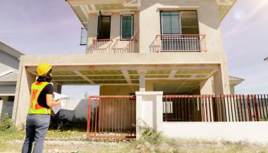 Üst düzey kadın mimar proje tasarısını elinde tutuyor. Projenin önündeki inşaat sahasında duruyor. İnşaatın ilerlemesine bakıyor..