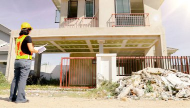 Üst düzey kadın mimar proje tasarısını elinde tutuyor. Projenin önündeki inşaat sahasında duruyor. İnşaatın ilerlemesine bakıyor..