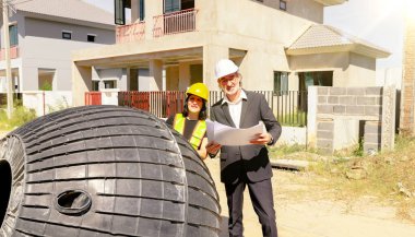 Erkek mimar ve kadın ustabaşı evin içindeki foseptiği ve kiri inceliyor ve inşaat halindeki yerli atık su arıtma projesinin planına bakıyor..