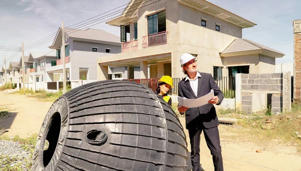 Erkek mimar ve kadın ustabaşı evin içindeki foseptiği ve kiri inceliyor ve inşaat halindeki yerli atık su arıtma projesinin planına bakıyor..