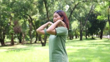 Genç Asyalı kadın sağlığına dikkat eder. Duruşunu ve omuzlarını yavaşça döndürerek gölgeli bir parkta egzersiz yapar..