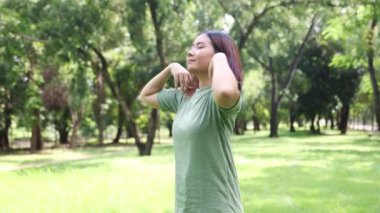 Genç Asyalı kadın sağlığına dikkat eder. Duruşunu ve omuzlarını yavaşça döndürerek gölgeli bir parkta egzersiz yapar..