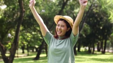 Güneşli bir sabah şapkası takan genç Asyalı bir portre neşeli, neşeli, neşeli, kendine güveni yüksek, pozitif, gölgeli ağaçlarla dolu bir bahçeye atlayan ve kameraya gülümseyen bir kadın..