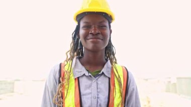 Bir inşaat sahasında çalışan Afro-Amerikan kadın işçinin portresi. Uzun saç örgüsü. Sert bir şapka takıyor..