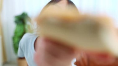 Neşeli küçük Asyalı kız kahvaltıda oturup lezzetli pizzalar yiyor. Elindeki bir dilim pizzayı gösteriyor ve onu mutlu bir şekilde yiyor..