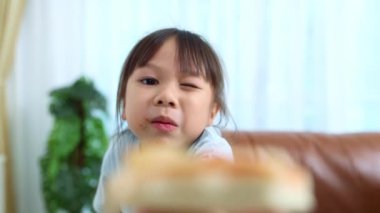 Neşeli küçük Asyalı kız kahvaltıda oturup lezzetli pizzalar yiyor. Elindeki bir dilim pizzayı gösteriyor ve onu mutlu bir şekilde yiyor..