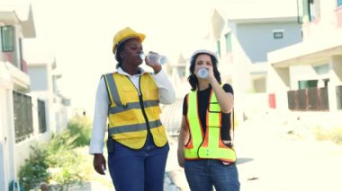 Mimarlar ve kadın işçiler, mola verirken gülümserken susuzluklarını gidermek için şişelerde temiz su içerek ayakta duruyorlar..