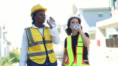 Mimarlar ve kadın işçiler, mola verirken gülümserken susuzluklarını gidermek için şişelerde temiz su içerek ayakta duruyorlar..
