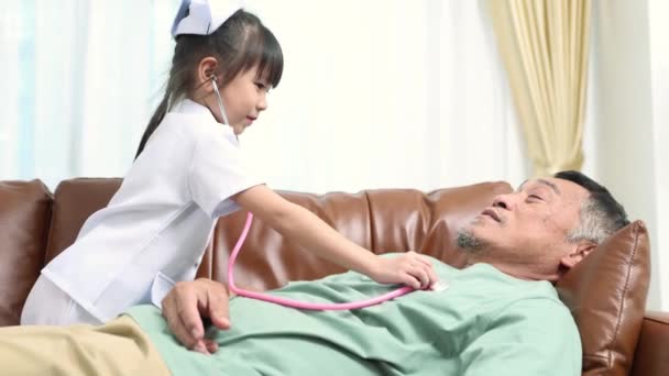 リトル看護師は 一緒に演奏し 楽しんでいる脈拍を聞くために医学的な歯科鏡を使用してソファーに横たわる病気のおじいちゃんと看護師を演じます — ストック動画