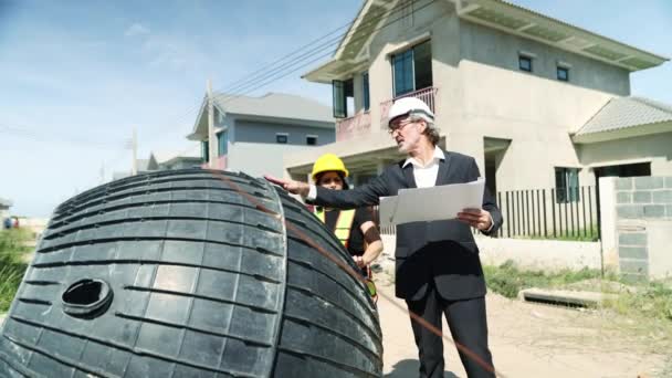 男性建築家と女性のフォアマンワーカーは 家の中のセプティックタンクと汚れを検査し 建設中の国内排水処理システムハウジングプロジェクトの青写真を見てください — ストック動画