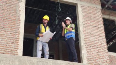 Kıdemli mimar emir verir ve inşaat projesinin altındaki ikinci kattaki konut projesinin planlarına göre ustabaşıyla yapılan görüşmeleri izler..